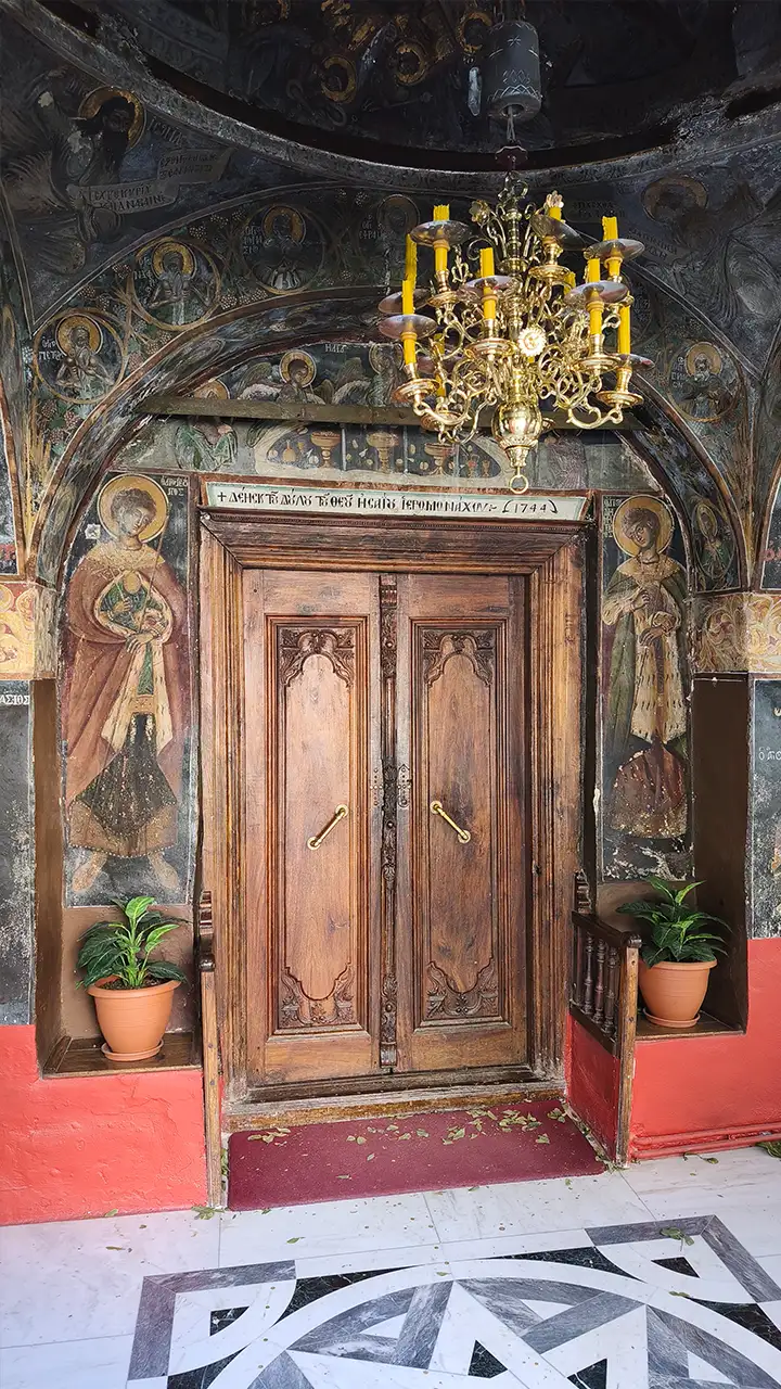 Деревянные двери входа в храм монастыря Кутлумуш на Афоне, окружённые фресками и золотой люстрой